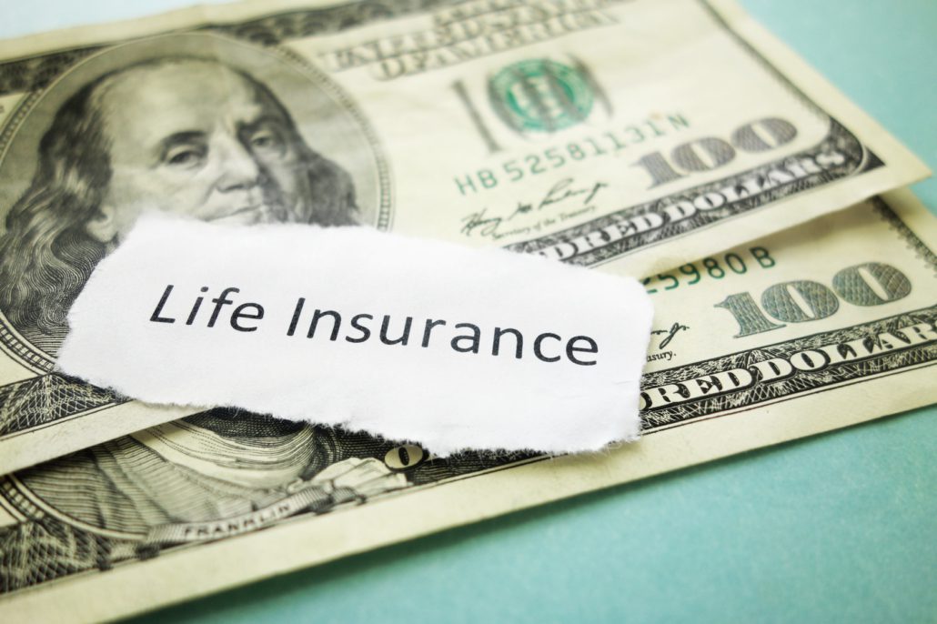 life insurance written on a page placed on top of two hundred dollar bills