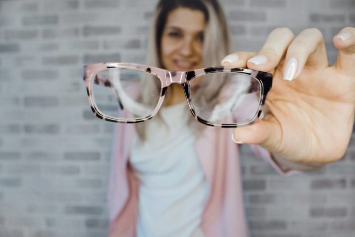 Woman holding eyeglasses in front of camera with a smile