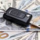 Car key fob resting on US dollar bills representing cost of auto insurance