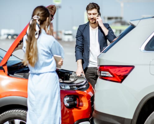 Man talking on phone beside damaged cars after a rear-end collision, woman standing nearby holding a phone.