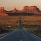Desert highway stretching toward Monument Valley rock formations at sunset