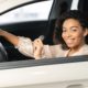 a woman sitting in her new car with key in hand and one hand on the steering wheel