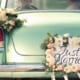 Rear of a vintage mint-green car decorated with flowers and a “Just Married” sign, indicating a wedding celebration.