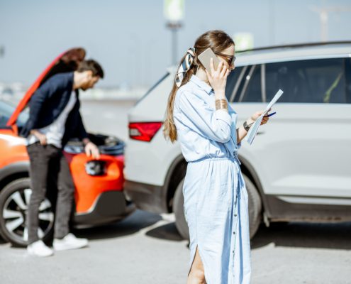 Woman on phone reviewing documents after car accident with damaged vehicles in background