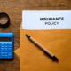 insurance policy papers in a brown envelop with a pen and calculator on the table