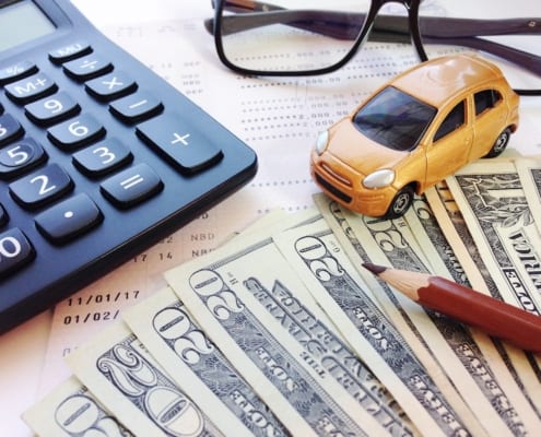 Calculator, toy car, eyeglasses, and U.S. dollar bills on financial paperwork, representing car expenses, budgeting, or auto insurance costs.