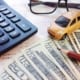 Calculator, toy car, eyeglasses, and U.S. dollar bills on financial paperwork, representing car expenses, budgeting, or auto insurance costs.
