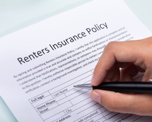 hand holding a pen filling renters insurance policy papers