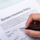 hand holding a pen filling renters insurance policy papers