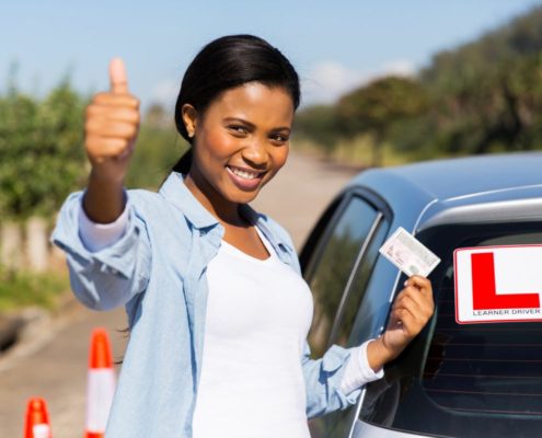 New driver holding license with learner sign on car window