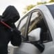 Masked person using a crowbar to break into a parked vehicle.