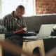 man writing in his notebook with a laptop on a table infront of him