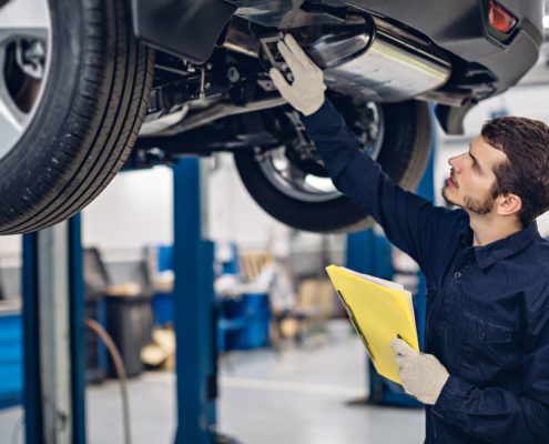 Auto mechanic inspecting car exhaust system on vehicle lift in repair shop