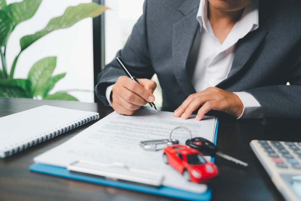 Man signing car insurance policy with car keys and red toy car on desk