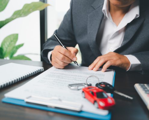 Man signing car insurance policy with car keys and red toy car on desk