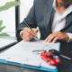 Man signing car insurance policy with car keys and red toy car on desk