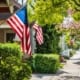 American flags displayed outside suburban homes on tree-lined residential street in the United States