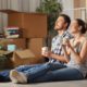 a couple sitting on the floor of their new house drinking tea surrounded by moving boxes