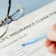 life insurance claim paper on a table with a hand filling it in