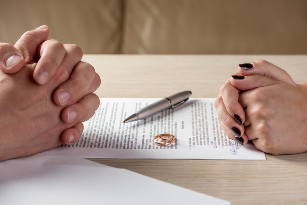 Couple sitting across from each other with divorce papers and wedding ring on table