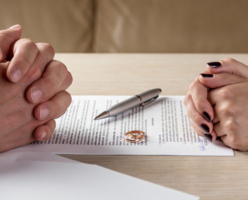 Couple sitting across from each other with divorce papers and wedding ring on table