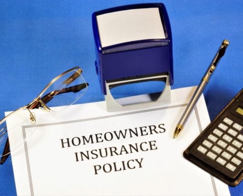 Homeowners insurance policy document on a desk with a calculator, pen, eyeglasses, and a stamp.