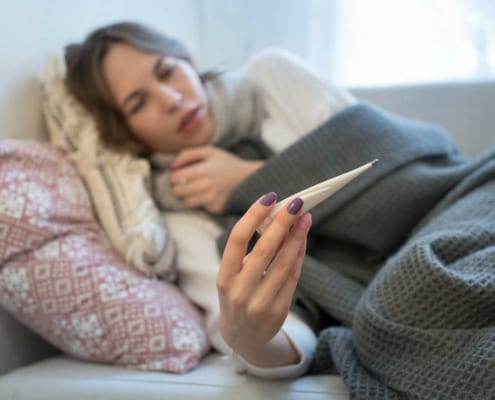 woman laying in a bed looking at a thermometer