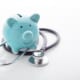 Blue piggy bank sitting inside a stethoscope on a white background.