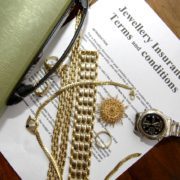 Gold jewelry and watch placed on jewellery insurance policy document with glasses and folder on desk