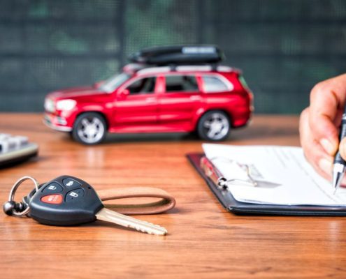 Signing car insurance policy with vehicle keys and model car on desk