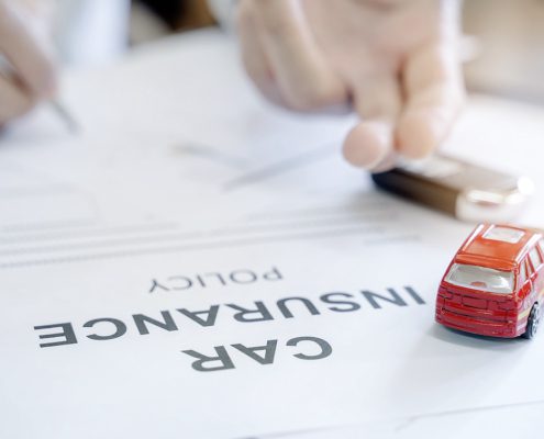 Person signing car insurance policy document with toy red car on form