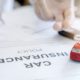 Person signing car insurance policy document with toy red car on form