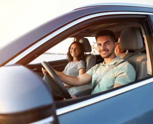 Smiling family sitting inside car with seatbelts on during sunset drive