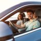 Smiling family sitting inside car with seatbelts on during sunset drive