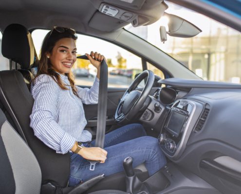 woman sitting in her car putting on her seat belt