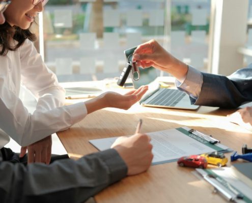 a car dealer handing the car keys of a new car to a couple while the husband signs the car insurance contract