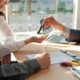 a car dealer handing the car keys of a new car to a couple while the husband signs the car insurance contract