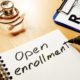 a notepad on a table with open enrollment written on it with doctor equipment on the table