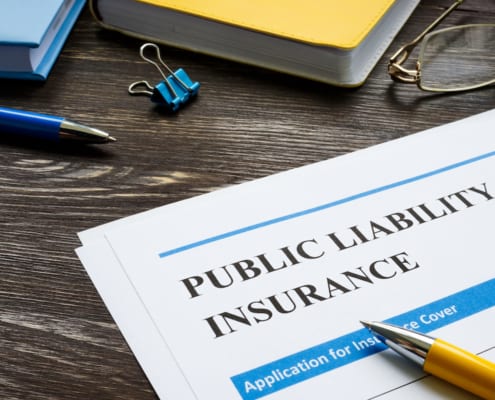 Public liability insurance document on desk with pen, notebook, glasses, and office supplies