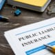 Public liability insurance document on desk with pen, notebook, glasses, and office supplies