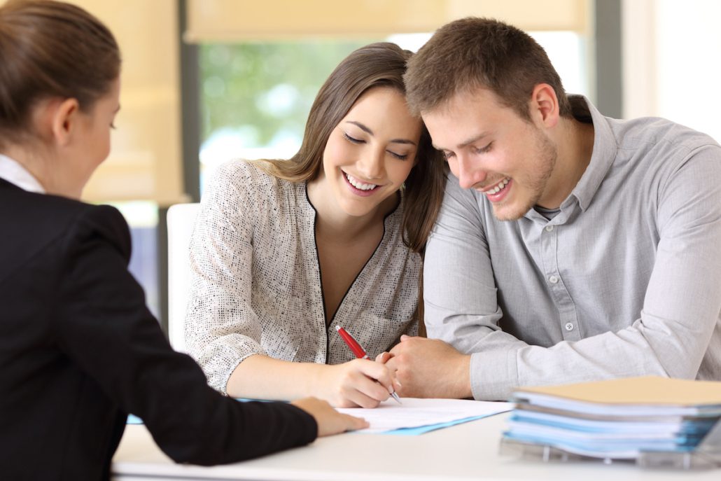 happy couple sitting with a insurance agent signing renters liability papers