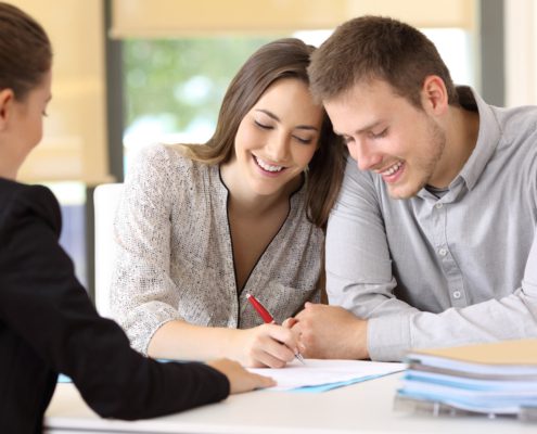 happy couple sitting with a insurance agent signing renters liability papers