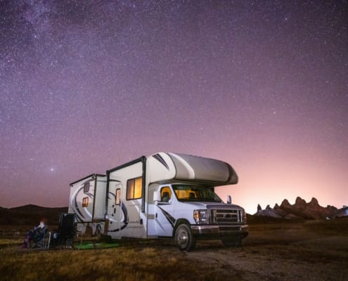 a rv parked in a field with a stary sky and the family sitting outside in lawn chairs
