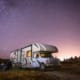 a rv parked in a field with a stary sky and the family sitting outside in lawn chairs