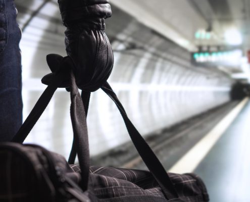 Person holding duffel bag on subway platform with train tracks in background