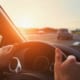 person hands on a steering wheel with a car on the highway in the background