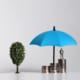 a model umbrella with a figure standing on coins under it and a toy tree next to it