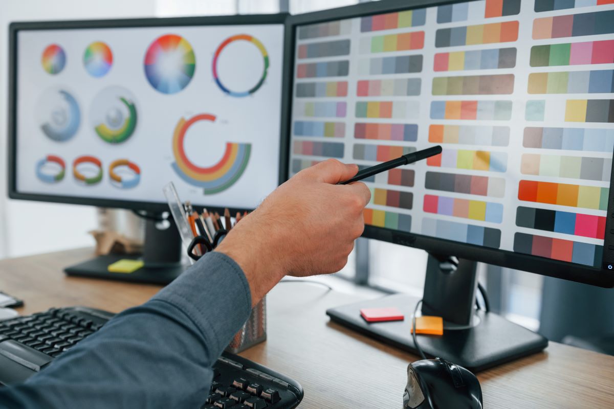 Graphic designer selecting brand color palette on dual monitors