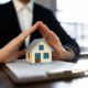 home insurance agent with papers Infront of him with a house figure on them with his hands over the house making a roof
