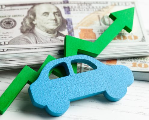 Blue wooden car shape and green upward arrow in front of stacked US $100 bills